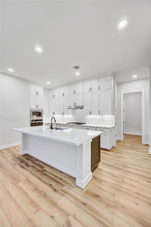 kitchen with stainless steel appliances, an island with sink, light hardwood / wood-style floors, and white cabinets