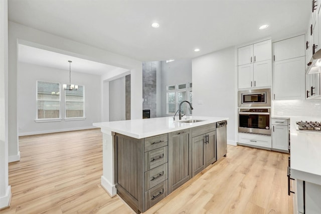 kitchen with hanging light fixtures, white cabinets, stainless steel appliances, an inviting chandelier, and light wood-type flooring