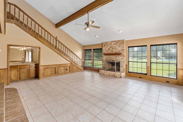 unfurnished living room featuring ceiling fan, beamed ceiling, light tile flooring, a fireplace, and high vaulted ceiling