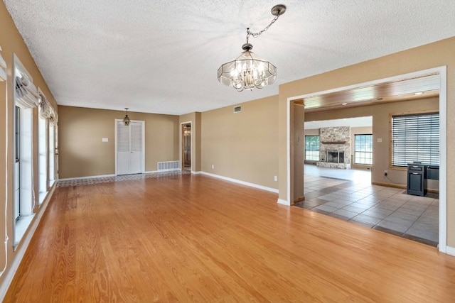 tiled empty room with a textured ceiling, a stone fireplace, and a chandelier