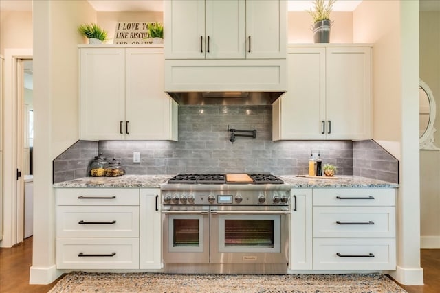 kitchen featuring range with two ovens, custom exhaust hood, backsplash, and light stone counters