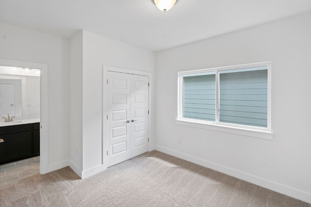 unfurnished bedroom featuring a closet, light colored carpet, sink, and ensuite bath