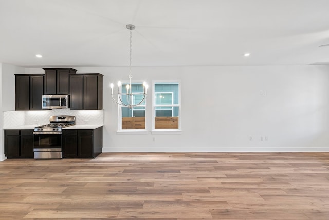 kitchen featuring pendant lighting, a chandelier, light hardwood / wood-style flooring, stainless steel appliances, and decorative backsplash