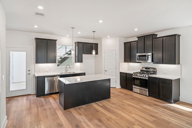 kitchen with tasteful backsplash, a kitchen island, sink, appliances with stainless steel finishes, and light hardwood / wood-style floors