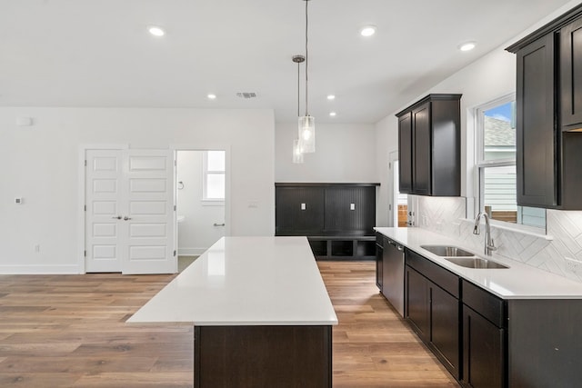 kitchen featuring pendant lighting, tasteful backsplash, a center island, sink, and light wood-type flooring