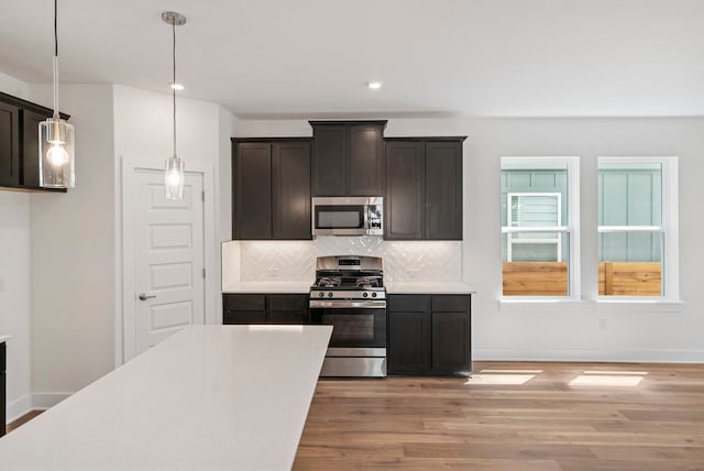 kitchen featuring hardwood / wood-style flooring, decorative light fixtures, stainless steel appliances, dark brown cabinets, and tasteful backsplash