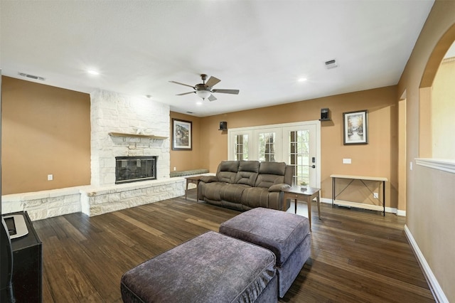 living room with dark hardwood / wood-style flooring, a stone fireplace, and ceiling fan