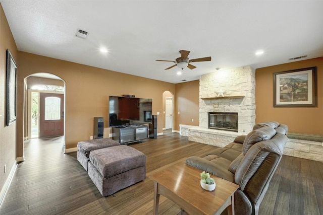 living room featuring dark hardwood / wood-style floors, ceiling fan, and a stone fireplace