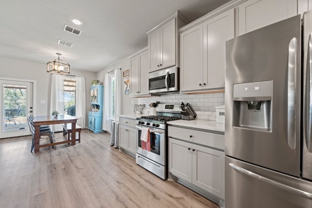 kitchen featuring pendant lighting, appliances with stainless steel finishes, light hardwood / wood-style flooring, backsplash, and an inviting chandelier