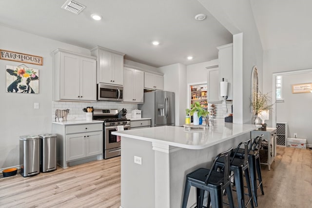 kitchen with appliances with stainless steel finishes, light hardwood / wood-style flooring, tasteful backsplash, and a breakfast bar