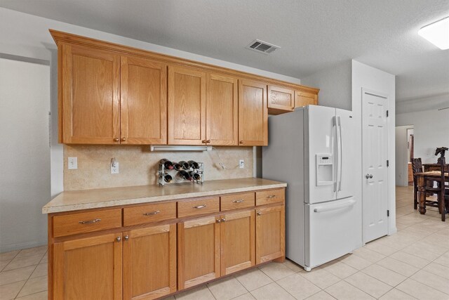 kitchen with backsplash, light tile patterned floors, white refrigerator with ice dispenser, and a textured ceiling