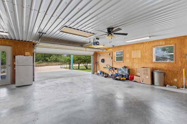 garage with wood walls, white fridge, a garage door opener, and ceiling fan