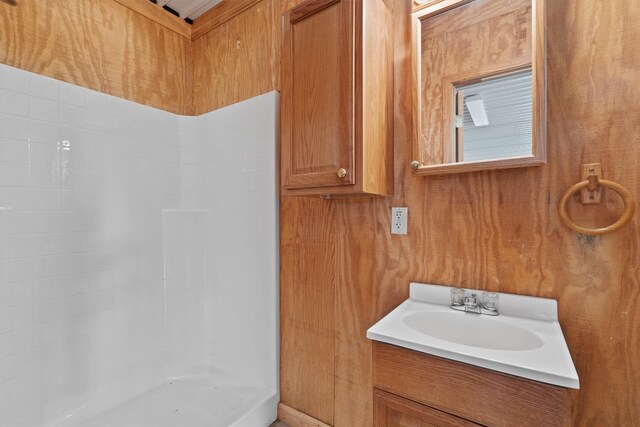 bathroom with vanity, wood walls, and a shower