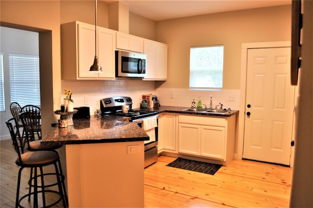 kitchen with tasteful backsplash, stainless steel appliances, sink, light wood-type flooring, and dark stone countertops