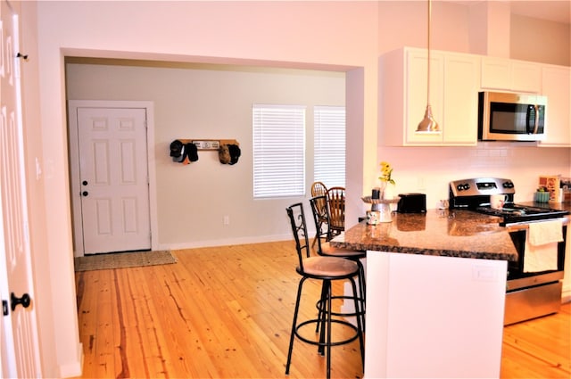 kitchen with a kitchen bar, electric stove, light wood-type flooring, dark stone countertops, and white cabinetry