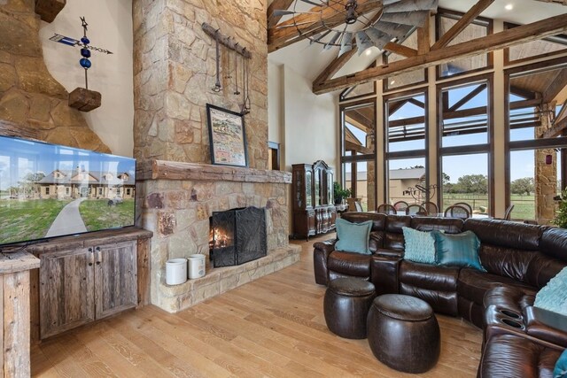 living room with a stone fireplace, beam ceiling, high vaulted ceiling, and light hardwood / wood-style floors