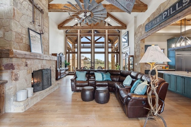 living room featuring ceiling fan, a stone fireplace, light hardwood / wood-style flooring, and beam ceiling