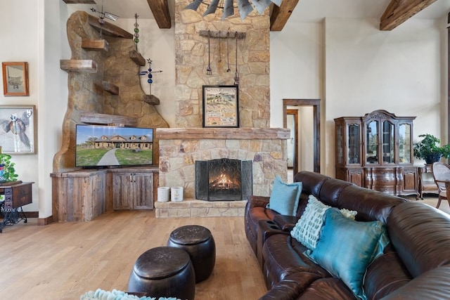 living room featuring a stone fireplace, light wood-type flooring, beamed ceiling, and a high ceiling