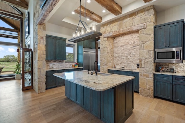 kitchen with backsplash, a kitchen island with sink, beamed ceiling, sink, and built in appliances