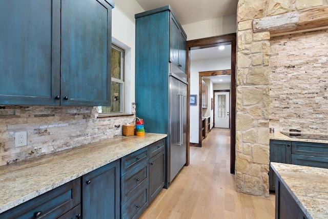 kitchen with light stone countertops, built in fridge, blue cabinets, and light wood-type flooring