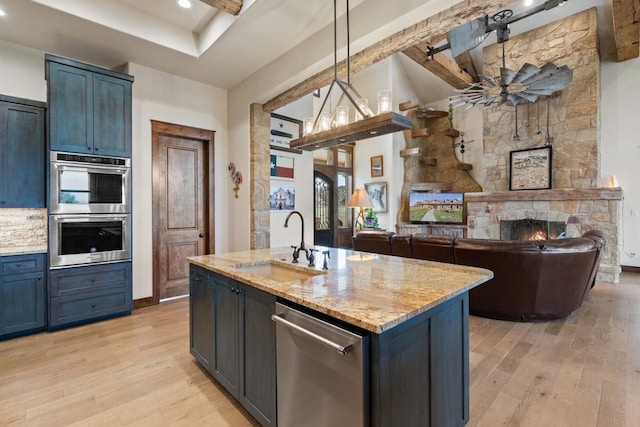 kitchen featuring pendant lighting, light hardwood / wood-style flooring, appliances with stainless steel finishes, sink, and light stone counters