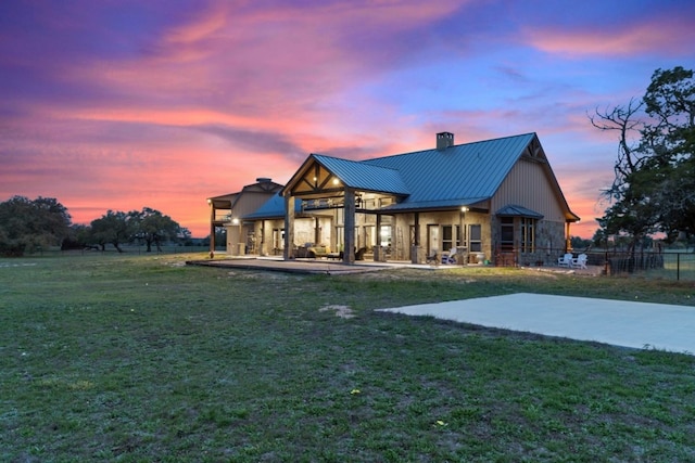 back house at dusk with a lawn and a patio