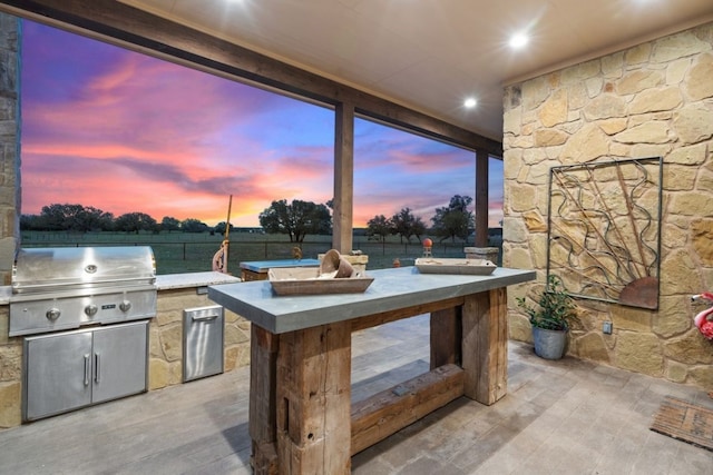 patio terrace at dusk featuring a grill and an outdoor kitchen