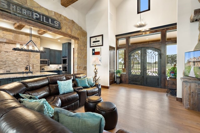 living room featuring a high ceiling, beamed ceiling, an inviting chandelier, light wood-type flooring, and french doors