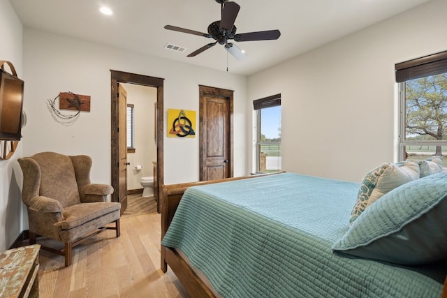 bedroom with ceiling fan, multiple windows, connected bathroom, and light hardwood / wood-style flooring