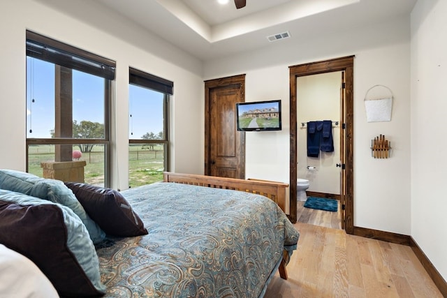 bedroom featuring a raised ceiling, connected bathroom, ceiling fan, and light hardwood / wood-style flooring