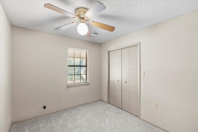 unfurnished bedroom featuring ceiling fan, a textured ceiling, light carpet, and a closet