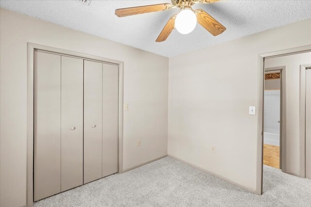 unfurnished bedroom featuring light colored carpet, a closet, ceiling fan, and a textured ceiling