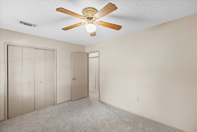 unfurnished bedroom with ceiling fan, a textured ceiling, light carpet, and a closet