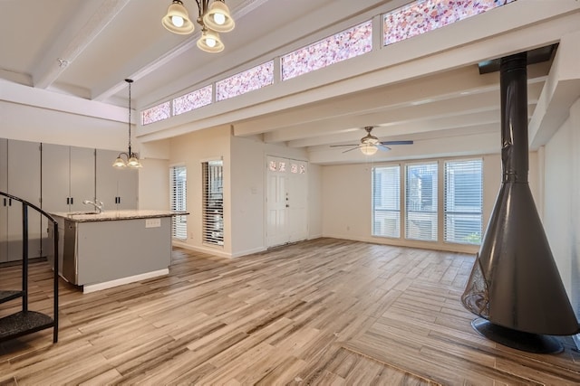 interior space with beam ceiling, ceiling fan with notable chandelier, sink, and light wood-type flooring