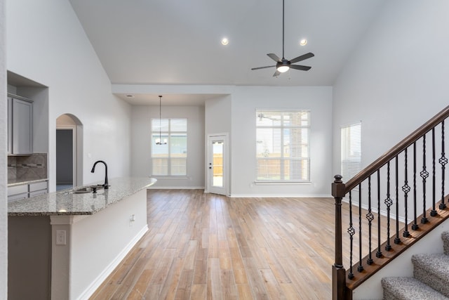 kitchen featuring light hardwood / wood-style floors, decorative light fixtures, high vaulted ceiling, ceiling fan with notable chandelier, and sink