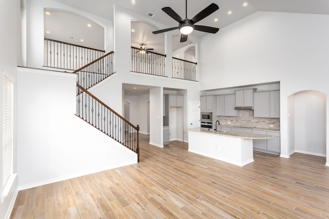 unfurnished living room featuring high vaulted ceiling, sink, ceiling fan, and light wood-type flooring