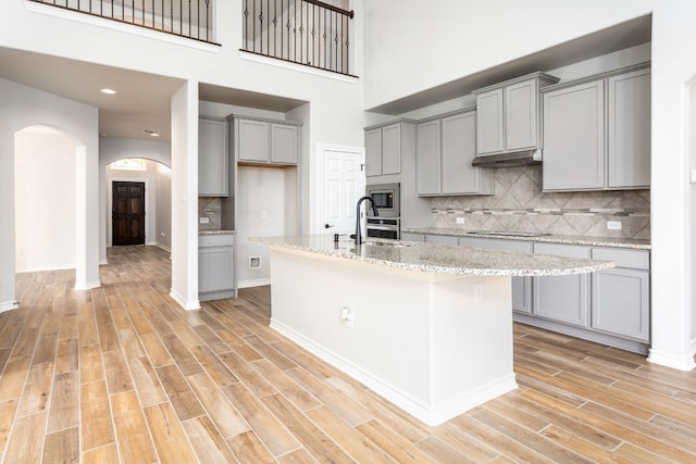 kitchen with backsplash, a center island with sink, gray cabinets, and light stone countertops