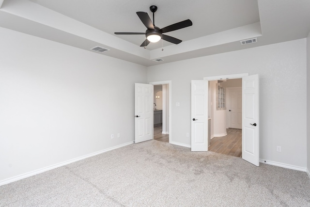 unfurnished bedroom with ceiling fan, light carpet, and a tray ceiling