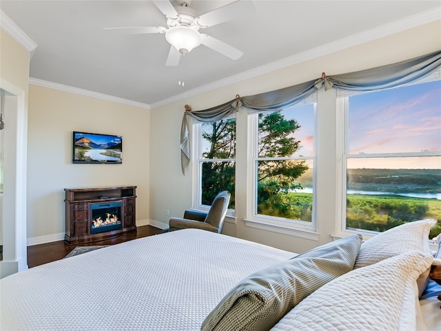 bedroom featuring dark wood-style floors, crown molding, a ceiling fan, a lit fireplace, and baseboards