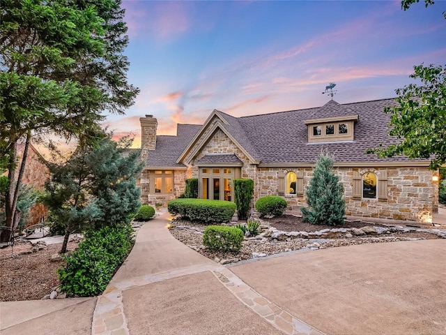 view of front of property with a shingled roof, stone siding, and a chimney