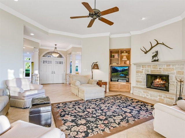 living area featuring ceiling fan, a stone fireplace, light tile patterned flooring, ornamental molding, and decorative columns