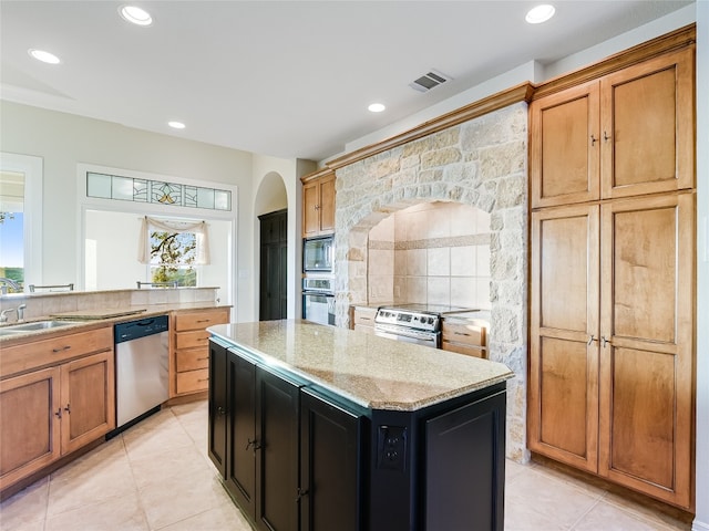 kitchen with a center island, stainless steel appliances, brown cabinetry, a healthy amount of sunlight, and light stone countertops