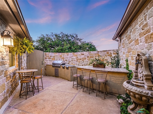 patio terrace at dusk featuring an outdoor bar, a grill, and area for grilling