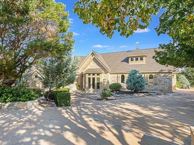 view of front of house with stone siding, roof with shingles, and french doors