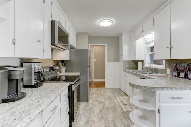 kitchen with appliances with stainless steel finishes, light countertops, white cabinetry, open shelves, and a sink