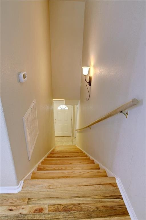 staircase featuring a towering ceiling, visible vents, and wood finished floors