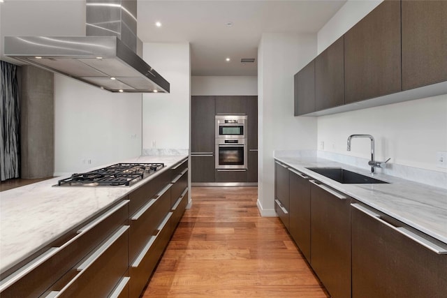 kitchen featuring appliances with stainless steel finishes, light hardwood / wood-style floors, wall chimney exhaust hood, light stone countertops, and sink