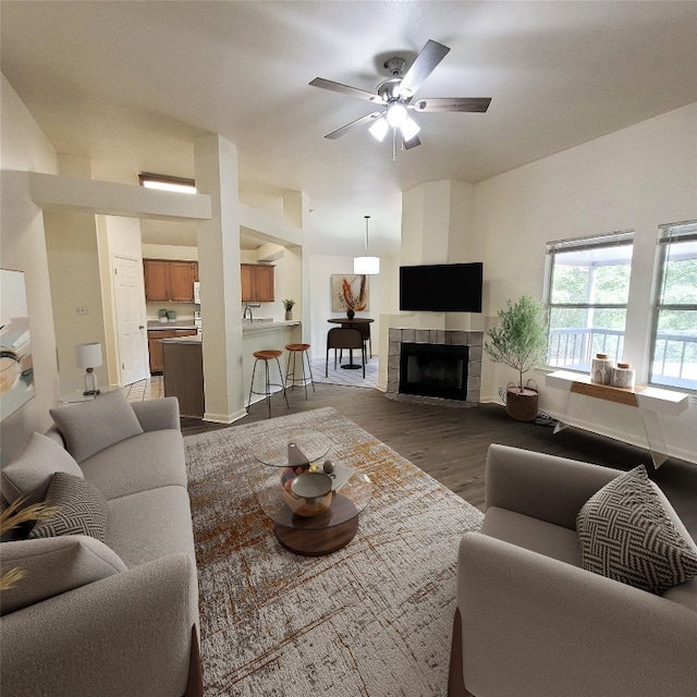 living room with a tiled fireplace, dark hardwood / wood-style floors, and ceiling fan