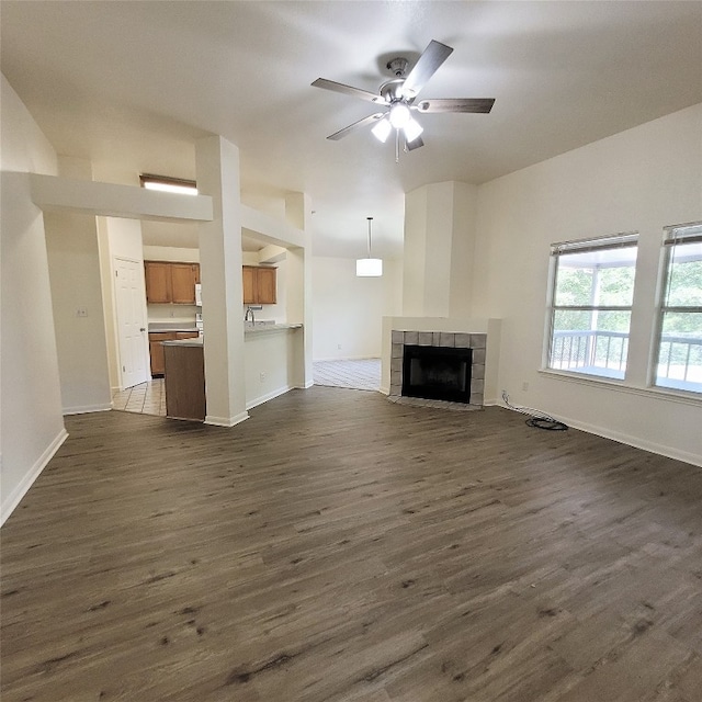 unfurnished living room featuring a tiled fireplace, ceiling fan, dark wood-type flooring, and sink