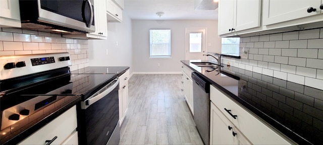 kitchen with appliances with stainless steel finishes, white cabinets, backsplash, light wood-type flooring, and sink